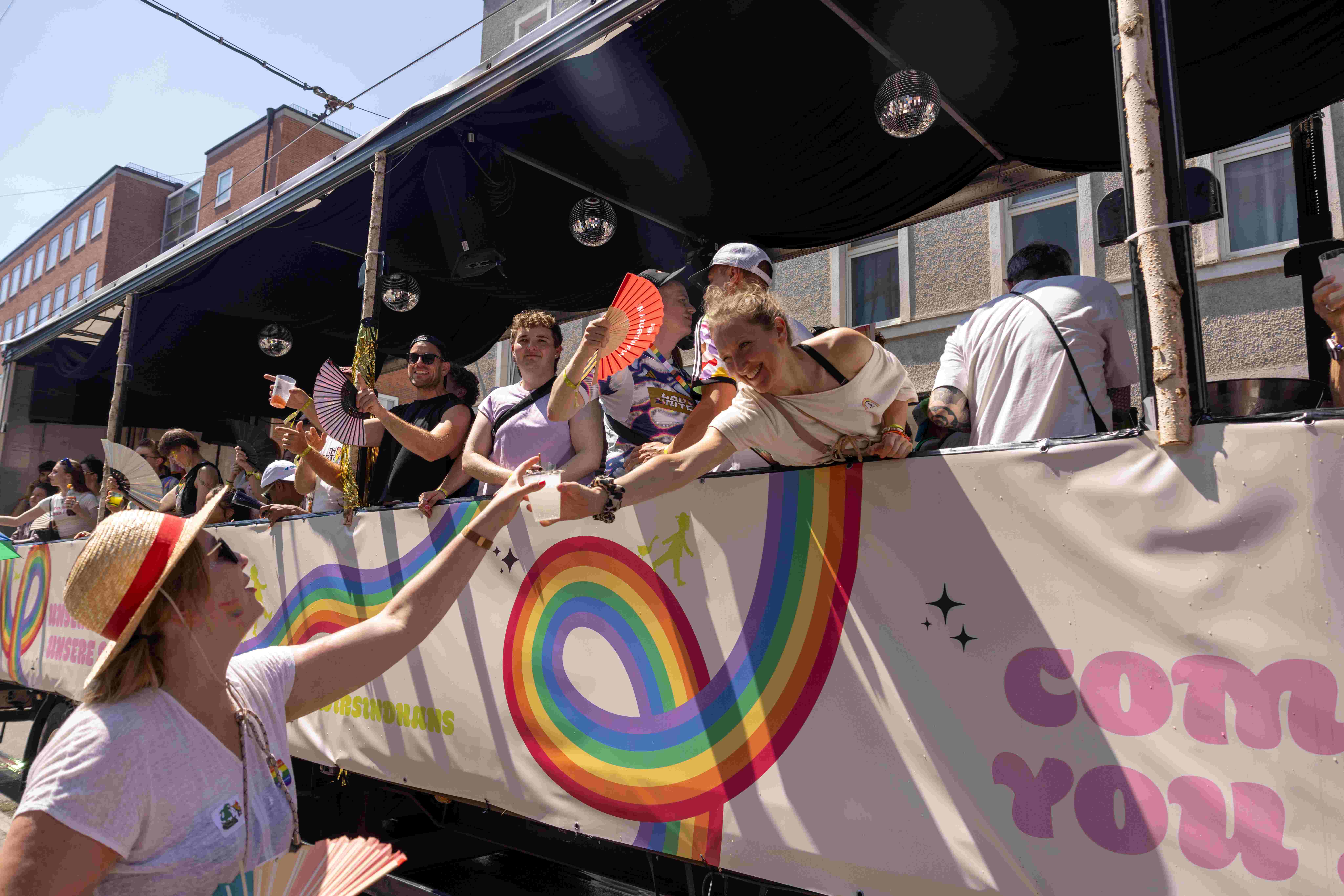 Eine Person vom CSD Truck reicht Wasser an das Publikum