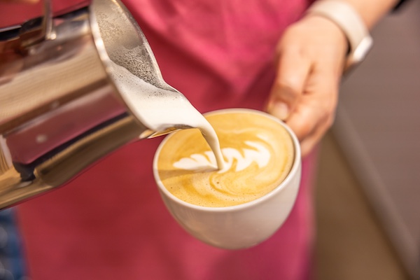 Barista gießt mit Milch ein Blatt in den Cappuccino